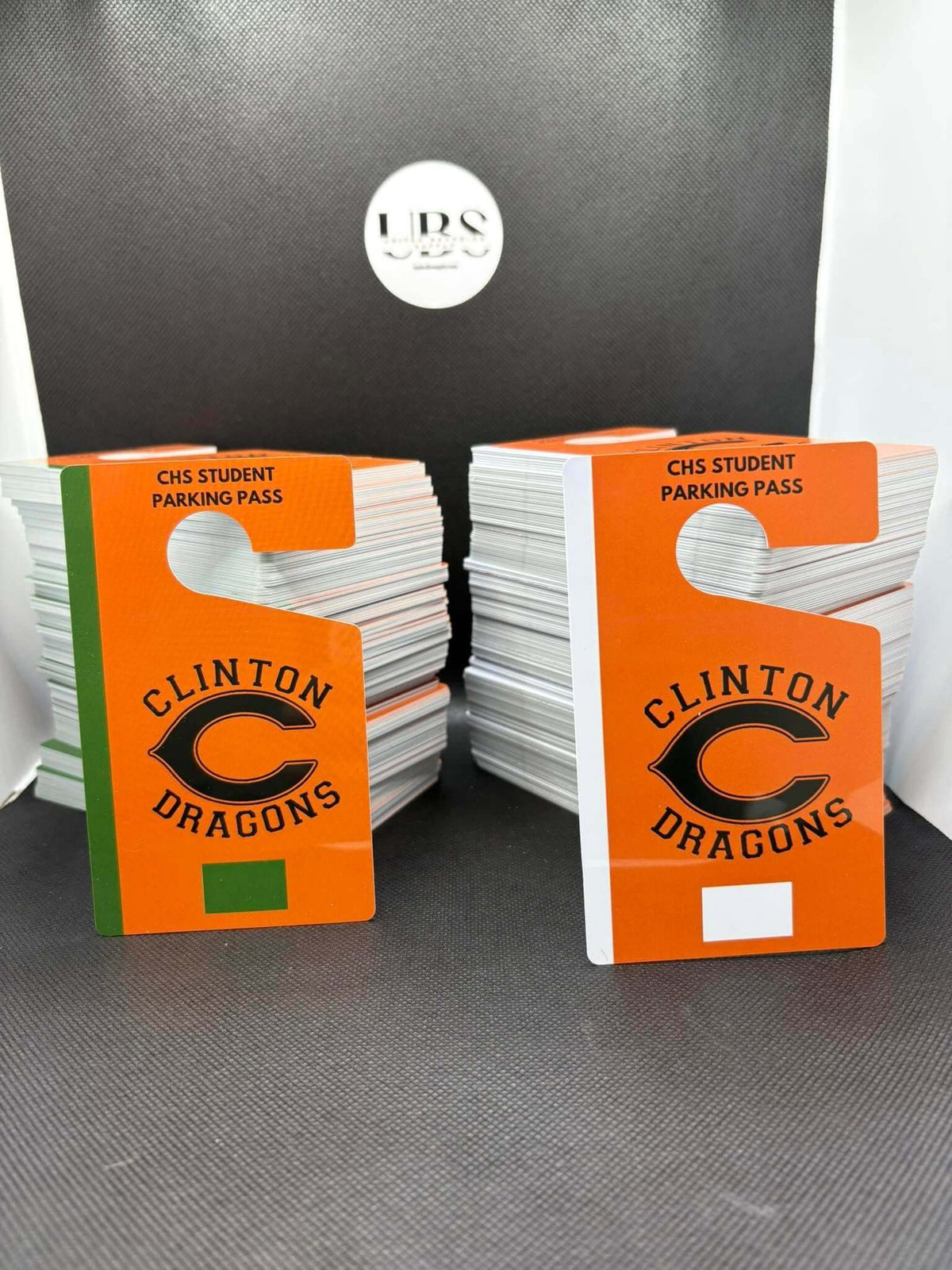 Two stacks of orange and white Clinton Dragons CHS Student Parking Pass hanger tags. Created by United Branding Supply.