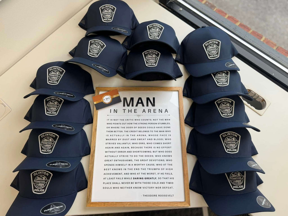 Navy caps embroidered with the Clinton Police Department Tennessee badge patch, by United Branding Supply.