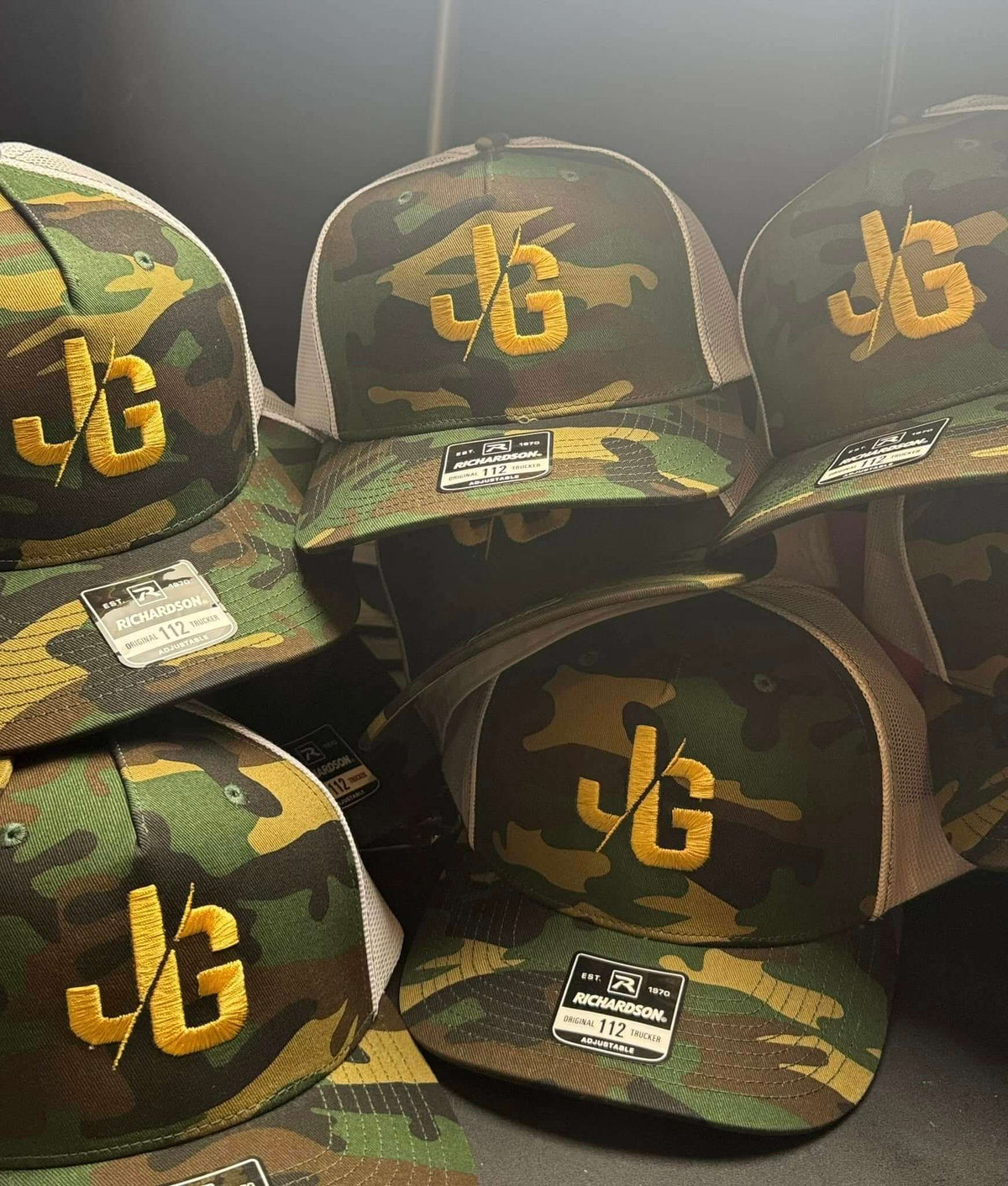 Camouflage trucker caps with a gold embroidered 'JG' logo, by United Branding Supply.