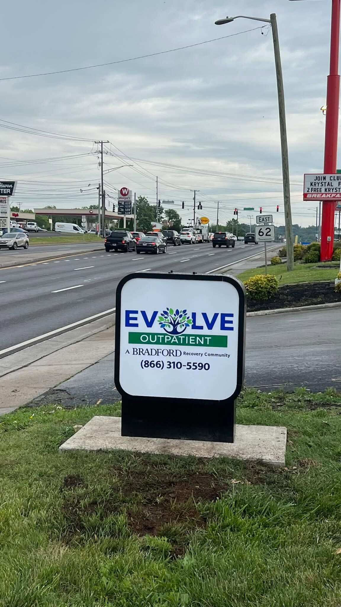 A freestanding outdoor sign for Evolve Outpatient, a Bradford Family Medicine Center, placed on grass beside a road with cars and utility poles in the background. Created by United Branding Supply.