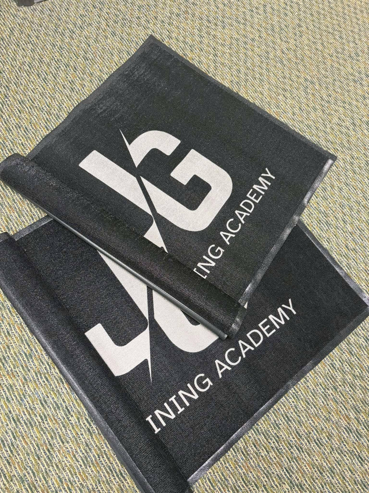 Two black embroidered JG Training Academy floor mats, by United Branding Supply