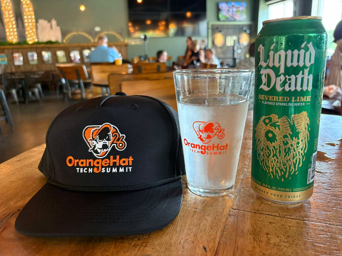 OrangeHat Tech Summit branded trucker cap and pint glass displayed on a table, by United Branding Supply